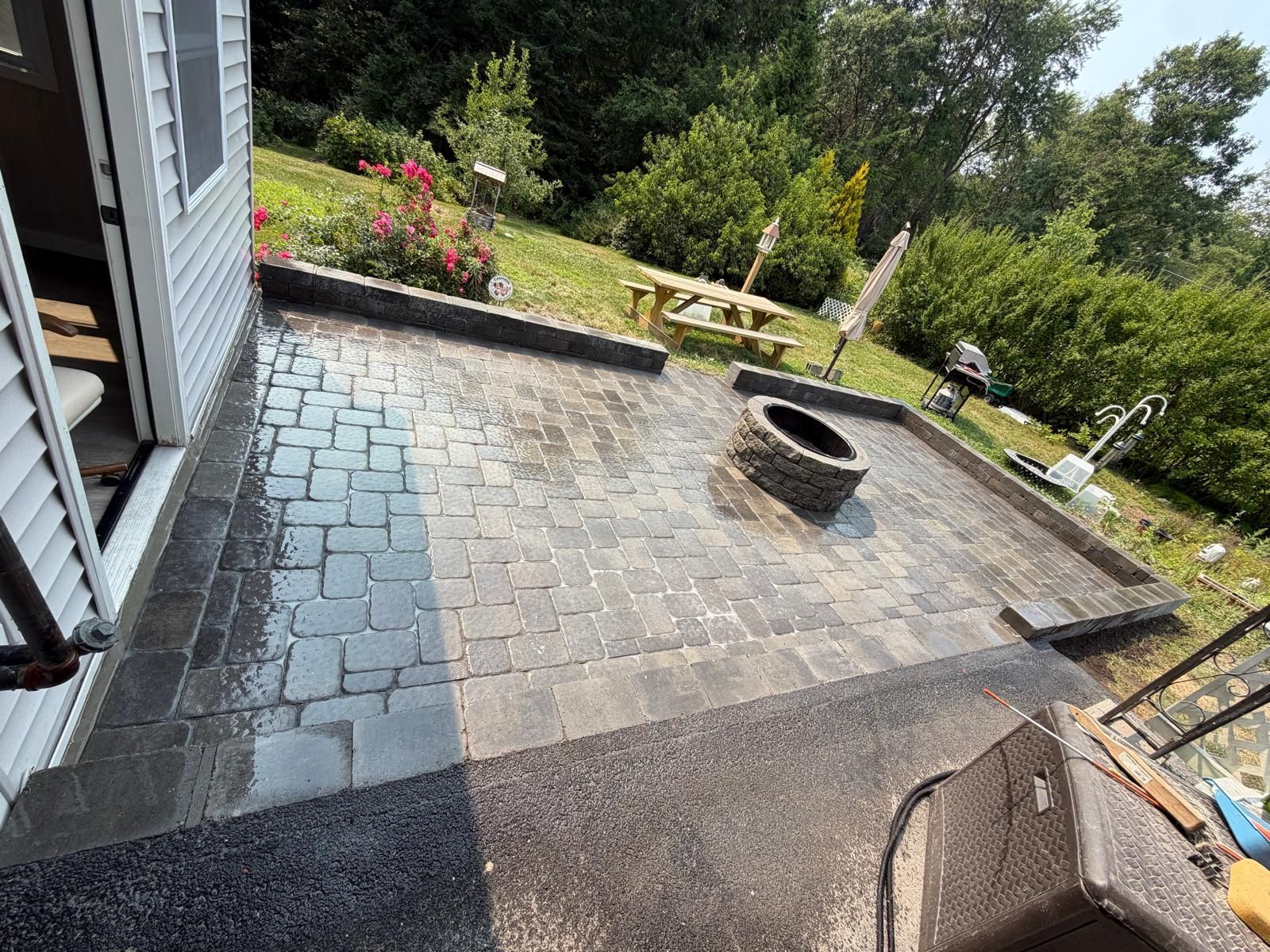 Backyard patio with stone pavers, a fire pit, steps, and garden beds beside a house
