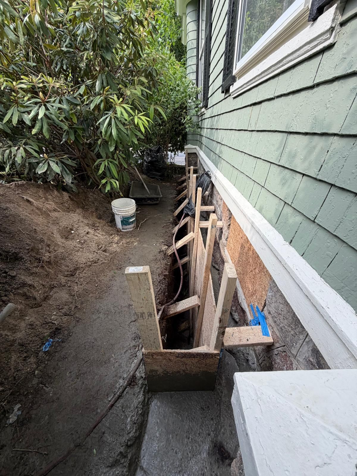 Narrow side yard with an open trench and exposed utility lines beside a green house during repair work