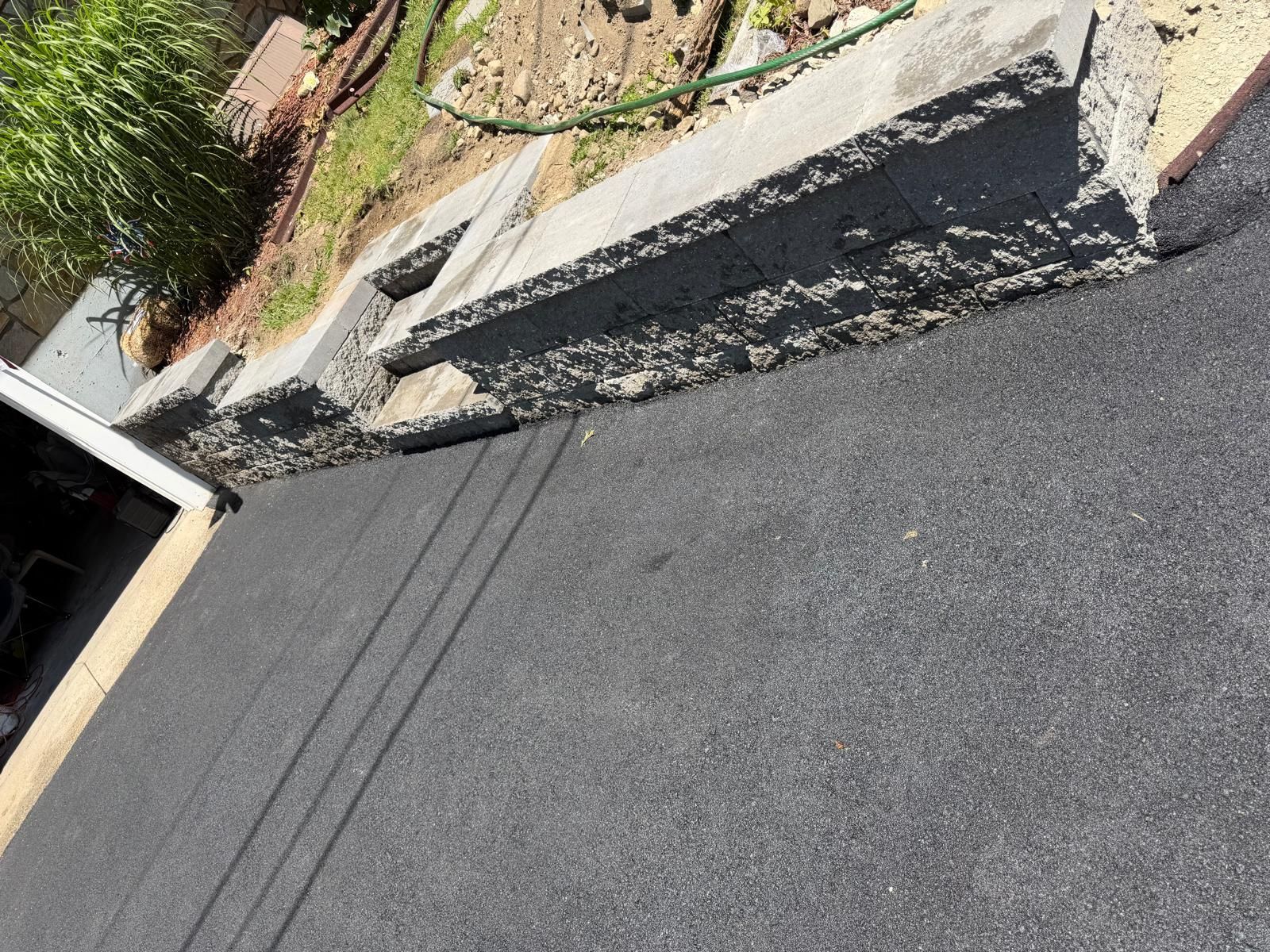 Asphalt driveway beside concrete curb and landscaped garden beds.