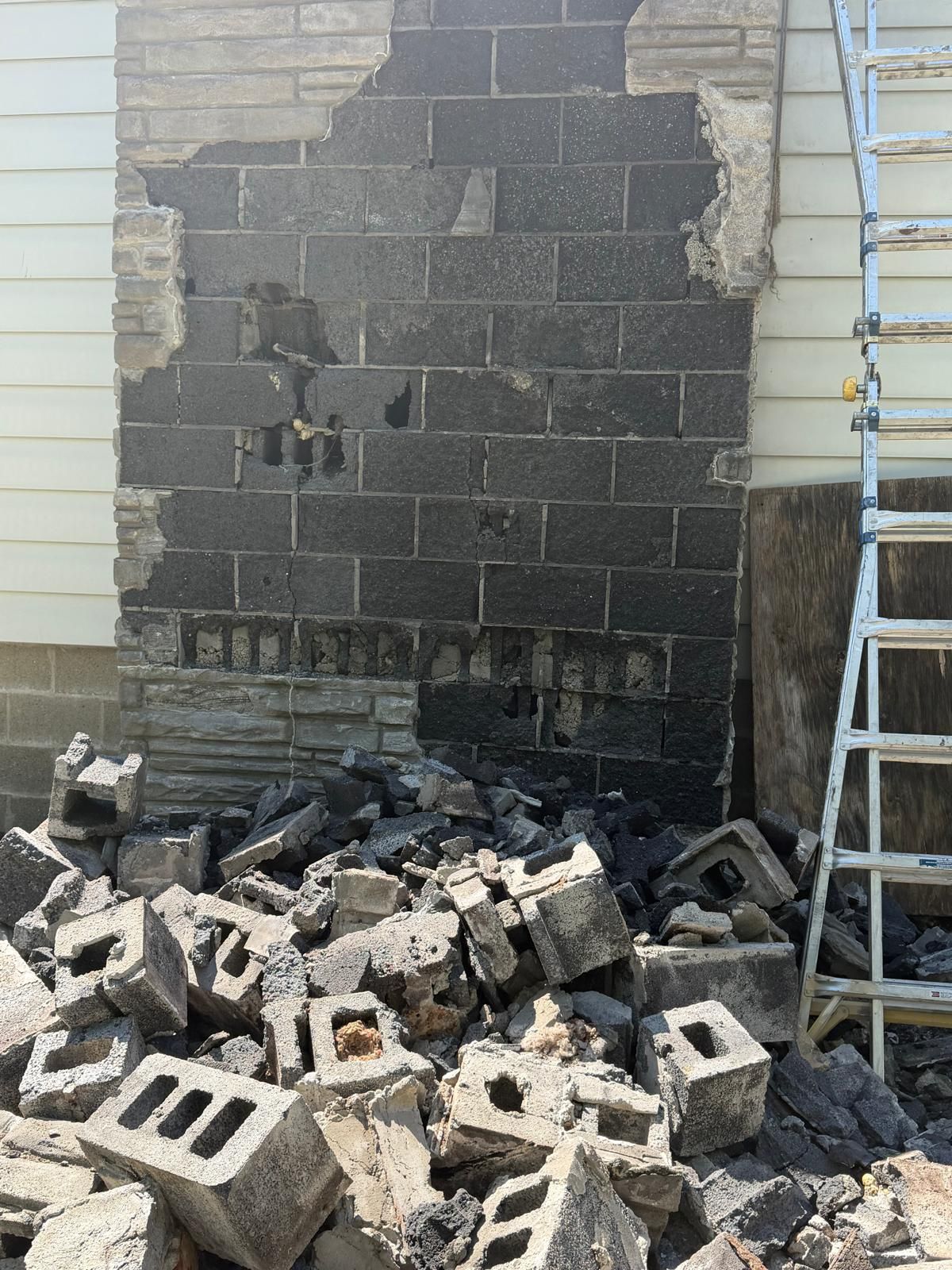 Partially demolished cinder block wall with rubble piled at the base and a ladder on the right