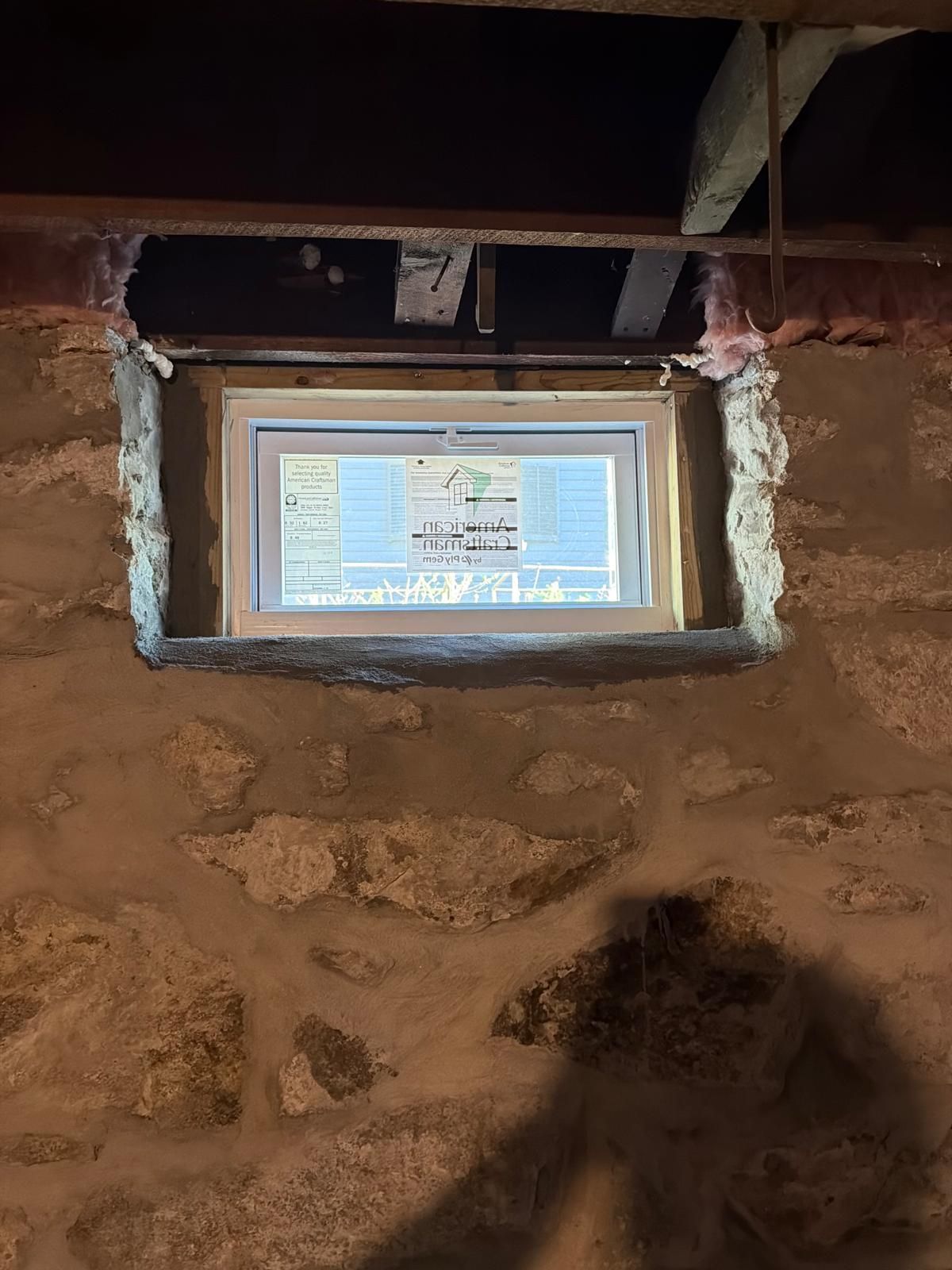Small basement window set in a rough stone wall with a light coming through.