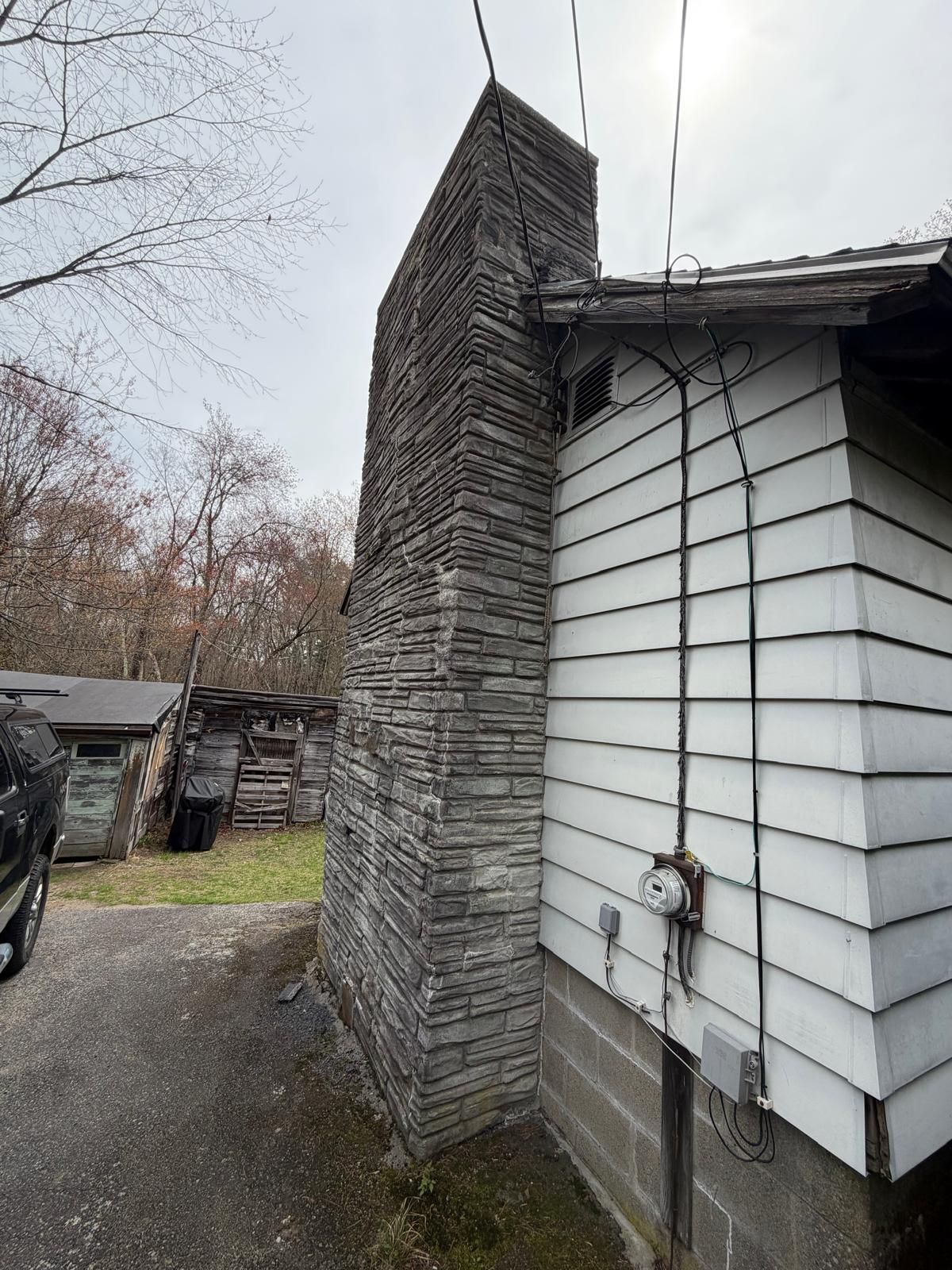 Side view of a white house with a tall stone chimney and a parked vehicle in the driveway
