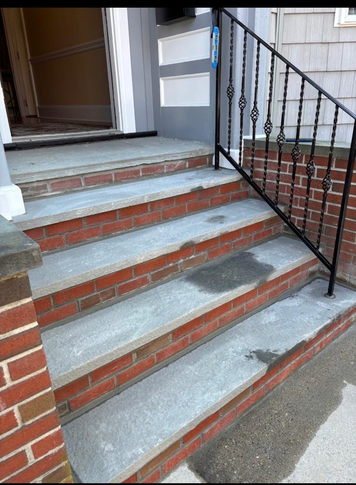 Brick front steps with gray concrete treads and a black metal handrail leading to a porch entrance