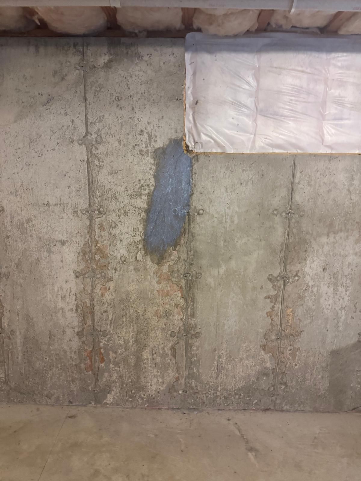 Concrete basement wall with a patched gray section and a white insulated panel near the ceiling.