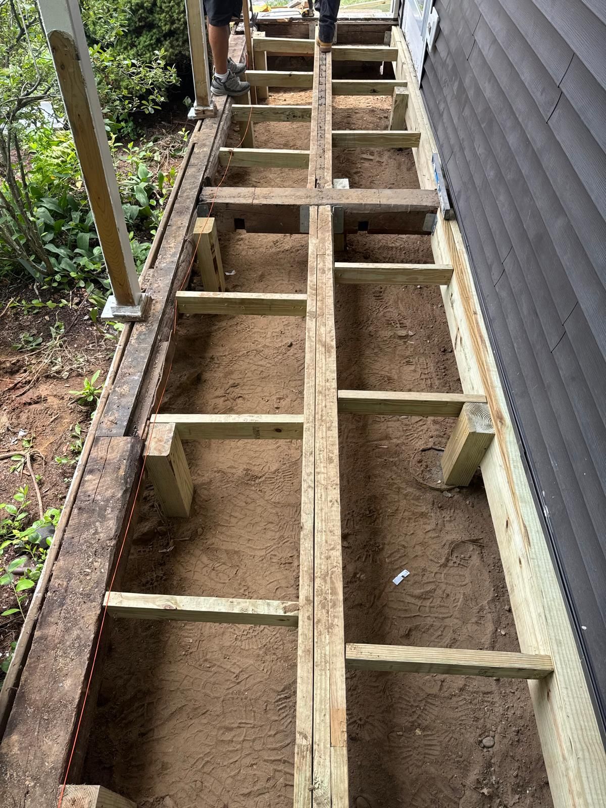 Wooden floor joists laid over a dirt trench beside a building wall during construction