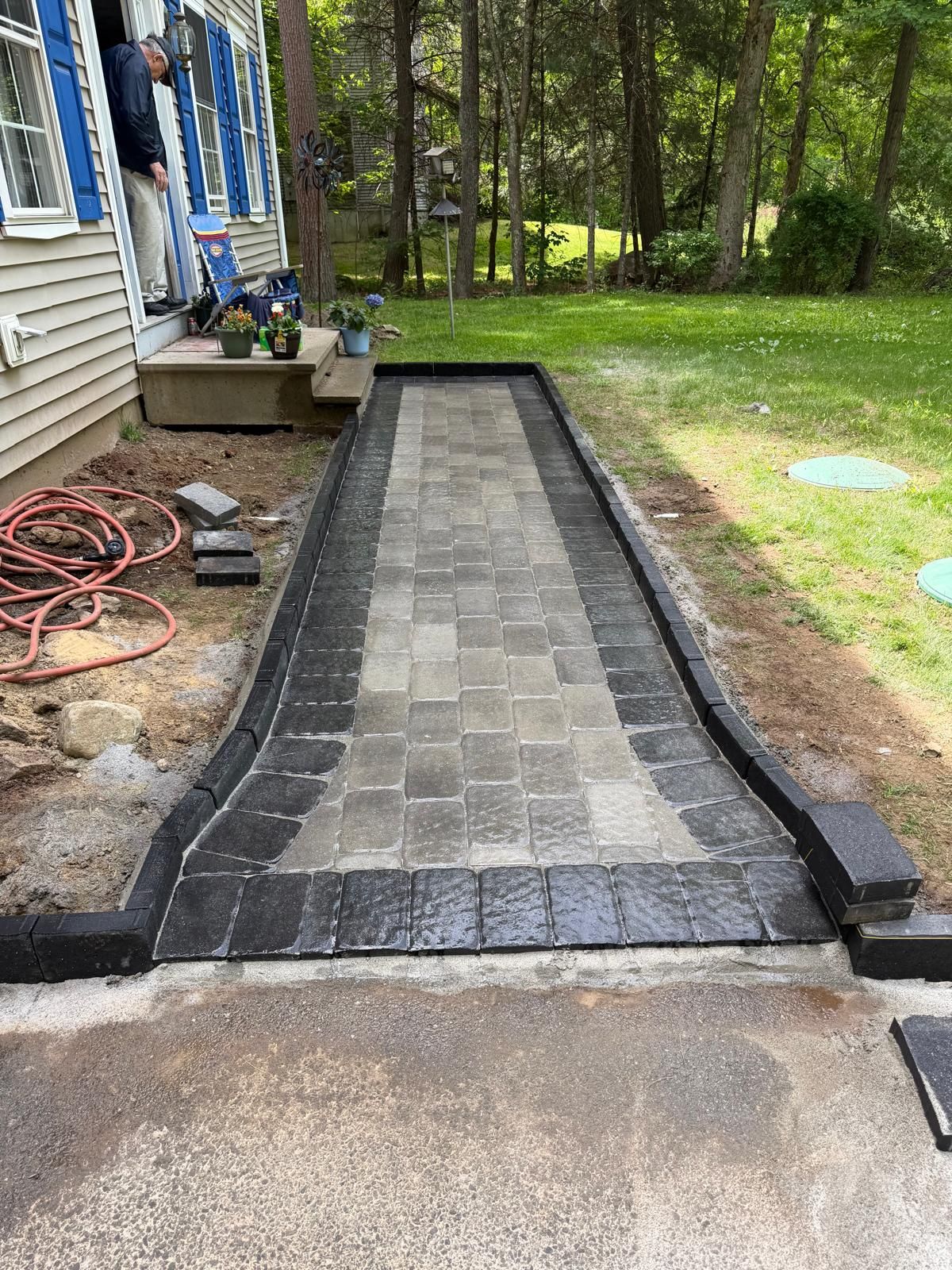 Paver walkway under construction beside a house, with black edging and a concrete base.