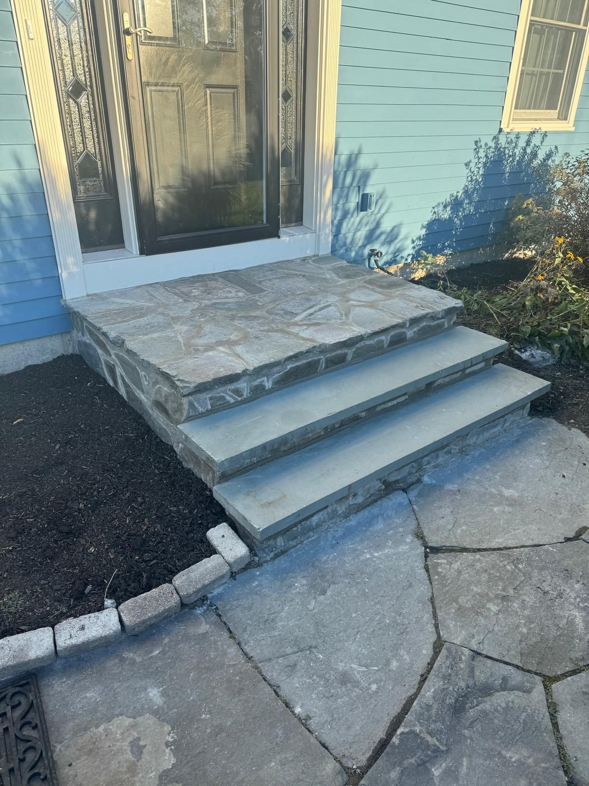 Front door with concrete steps and a small stone landing beside a blue house