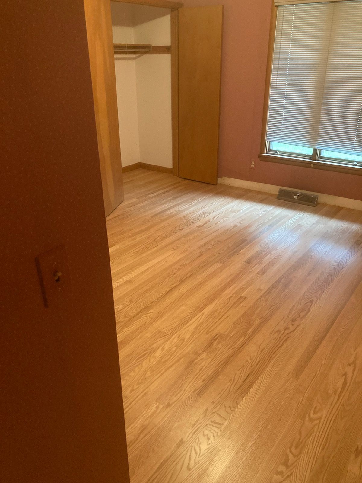 A bedroom with hardwood floors and a window.