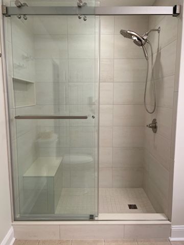 A modern tiled walk-in shower with a glass sliding door, a hand-held showerhead, and a built-in stone bench.