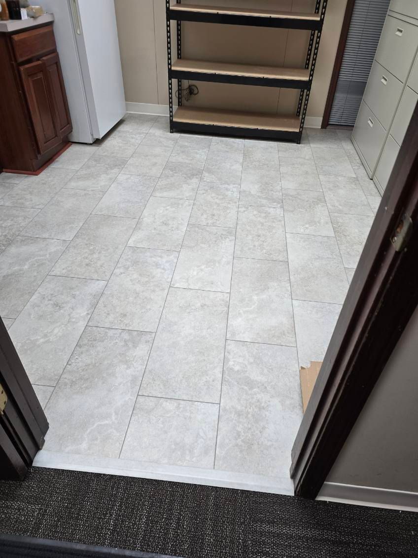 A view from a doorway looking into a room with light-colored, rectangular floor tiles and metal shelving.