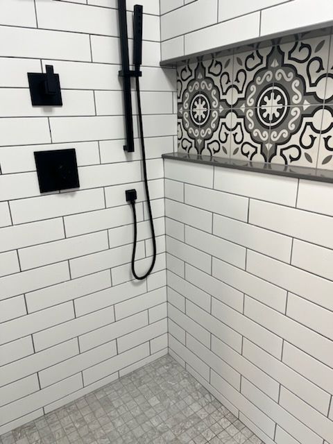 A shower interior featuring white subway tiles, a black shower head and controls, and a decorative patterned niche shelf.