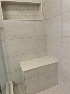 A neutral-toned tiled shower featuring a built-in bench seat and a recessed wall niche for toiletries.