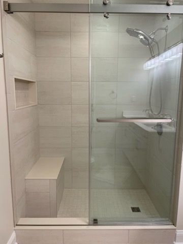 A walk-in shower with light-colored wall tiles, a built-in bench, a sliding glass door, and a modern shower head.