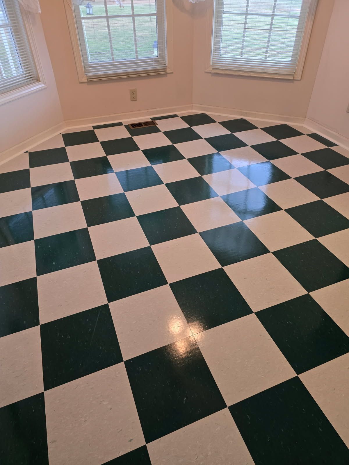 A sunlit room featuring a green and white checkered floor, positioned in front of two large windows.