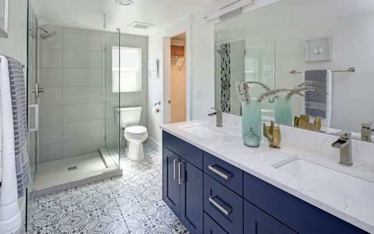 Modern bathroom with blue vanity, large mirror, glass shower, and patterned floor.