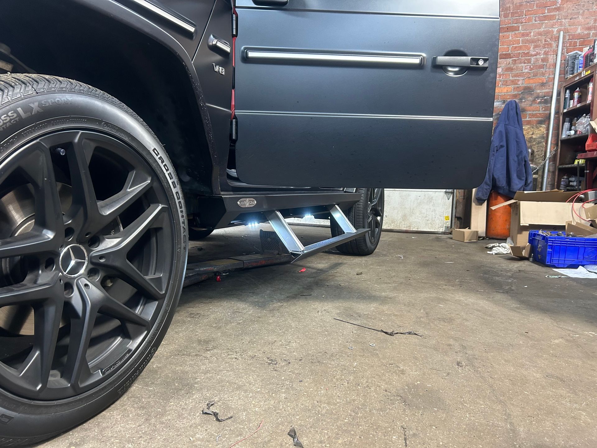 A black mercedes benz is parked in a garage with its doors open.