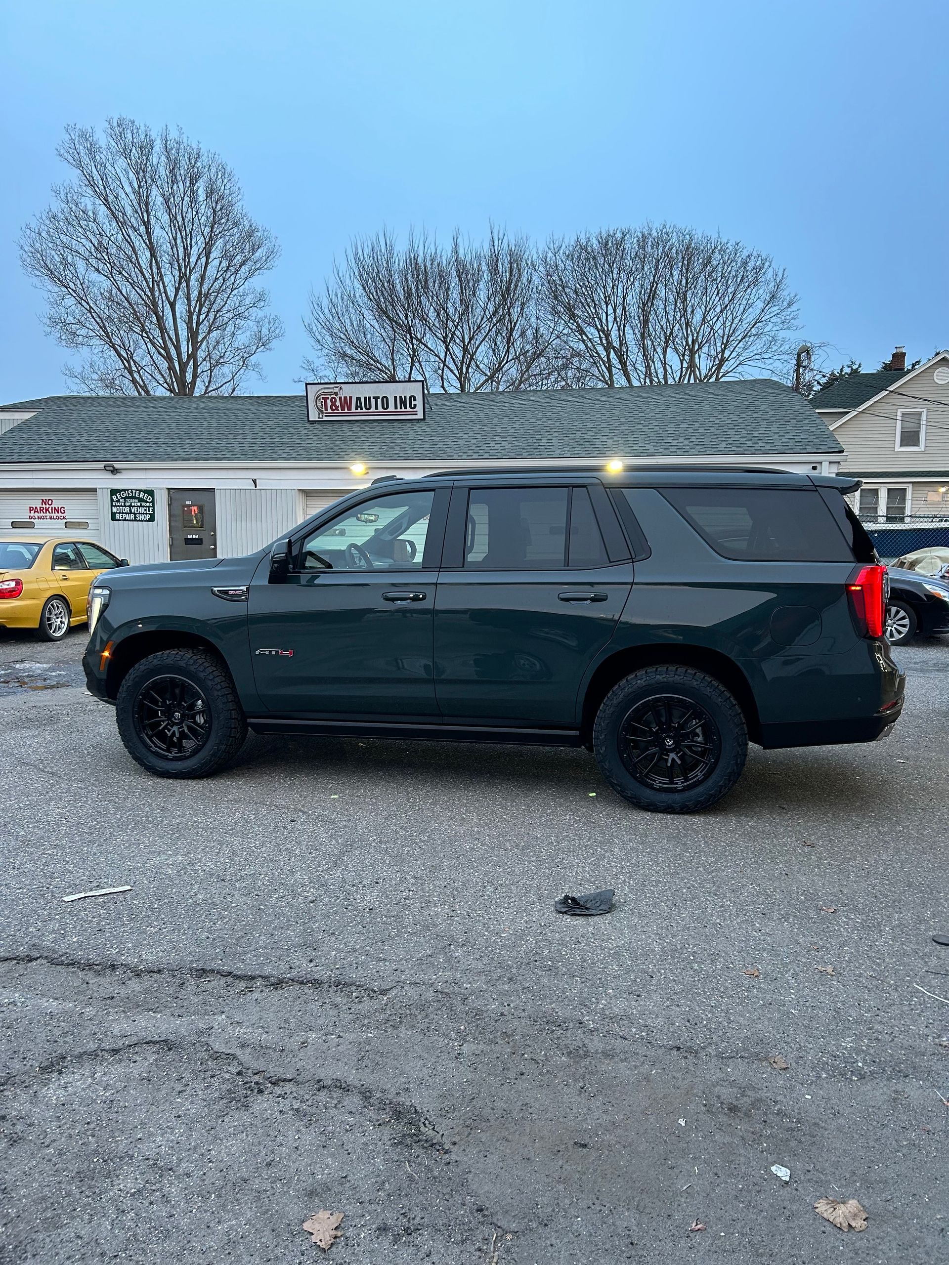 A black suv is parked in a gravel lot in front of a building.