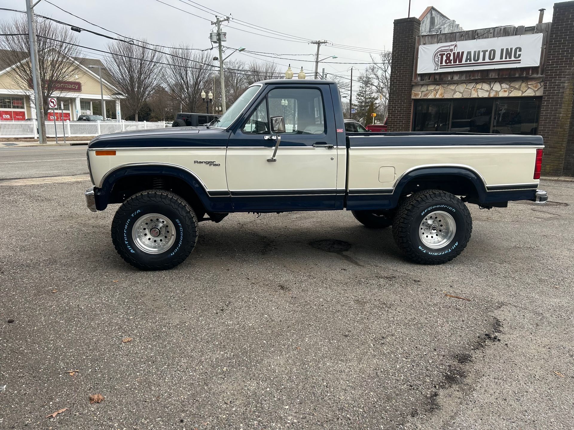 A white and blue pickup truck is parked in front of a building.