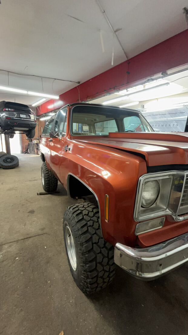 A red truck is parked in a garage next to a black car