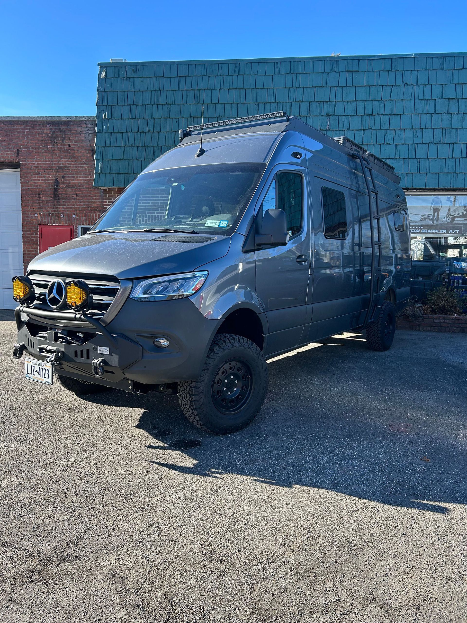 A gray van is parked in a gravel lot in front of a building