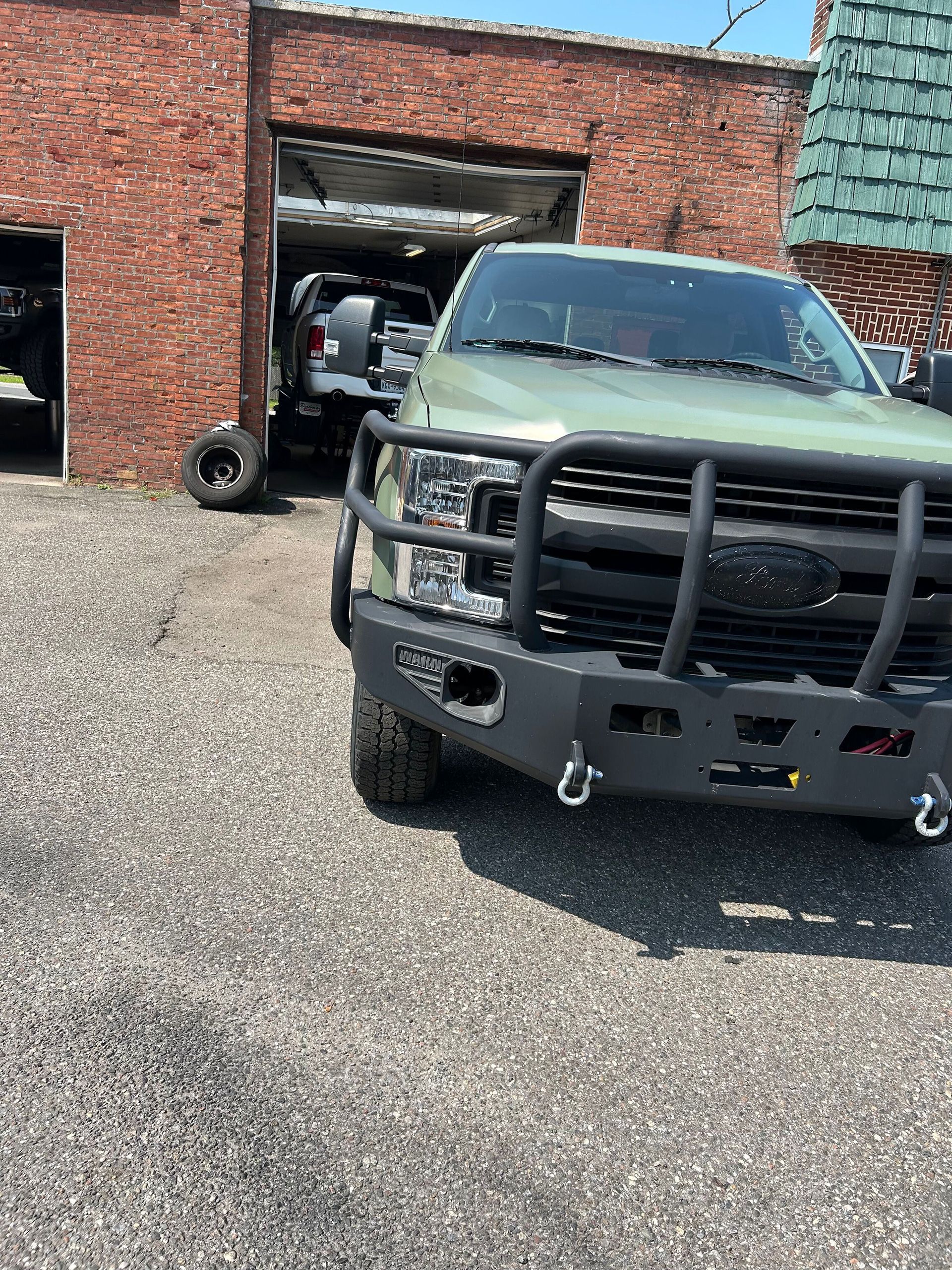 A green truck with a black bumper is parked in front of a brick building