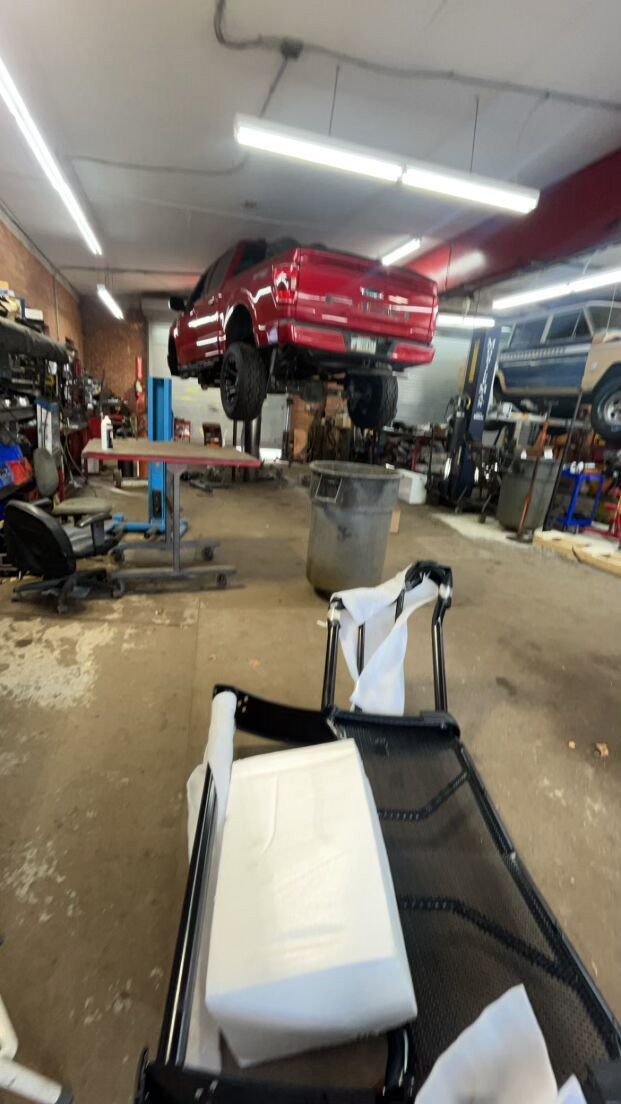 A red car is sitting on a lift in a garage for customization