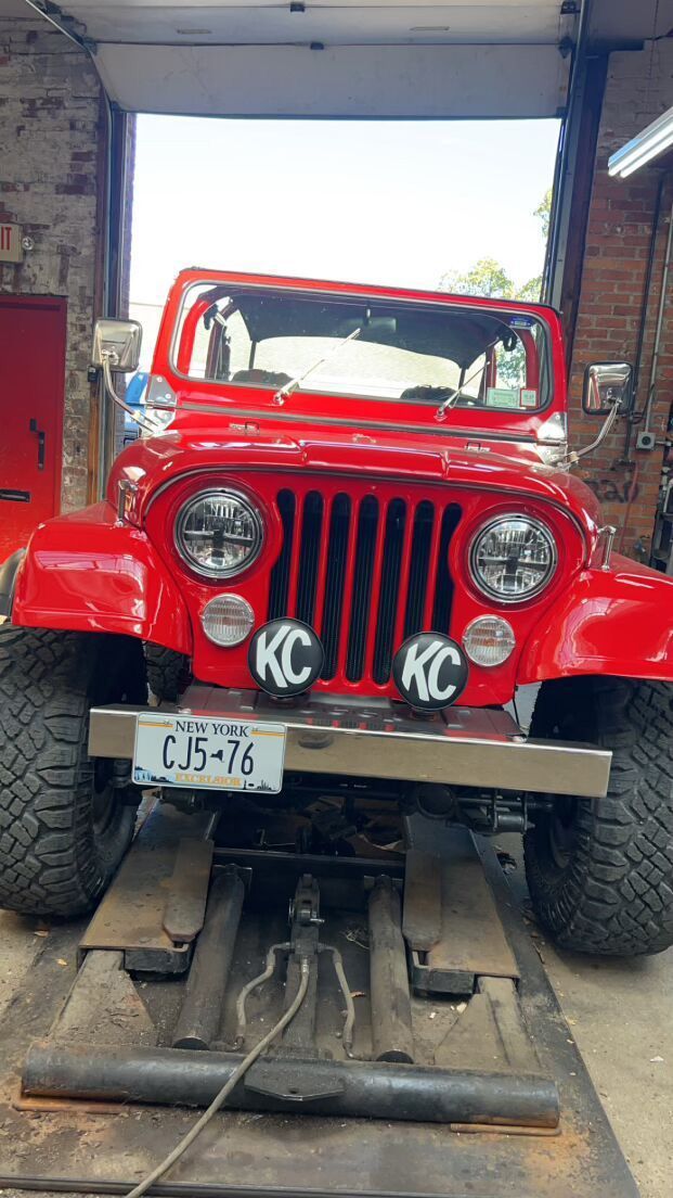 A red Jeep is sitting on a lift in a garage for customization