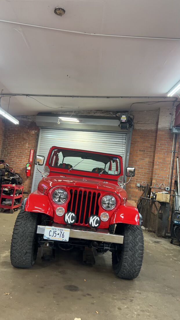 A red Jeep is parked in a garage for customization
