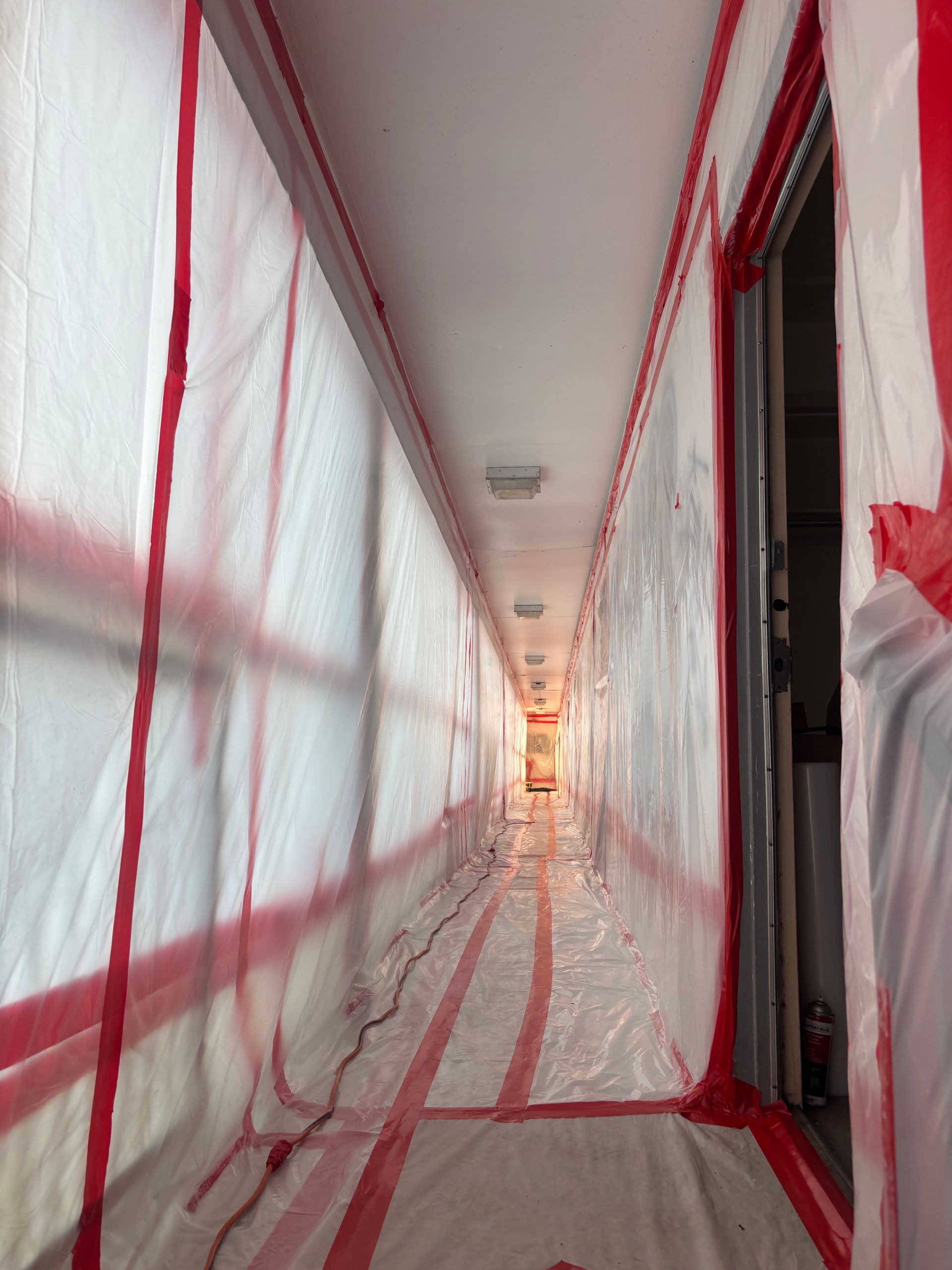 A long hallway covered in plastic and red tape.