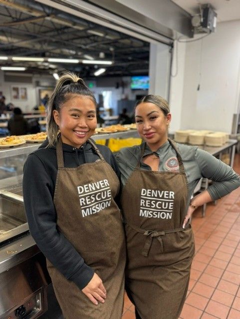 Two women wearing aprons are standing next to each other in a kitchen