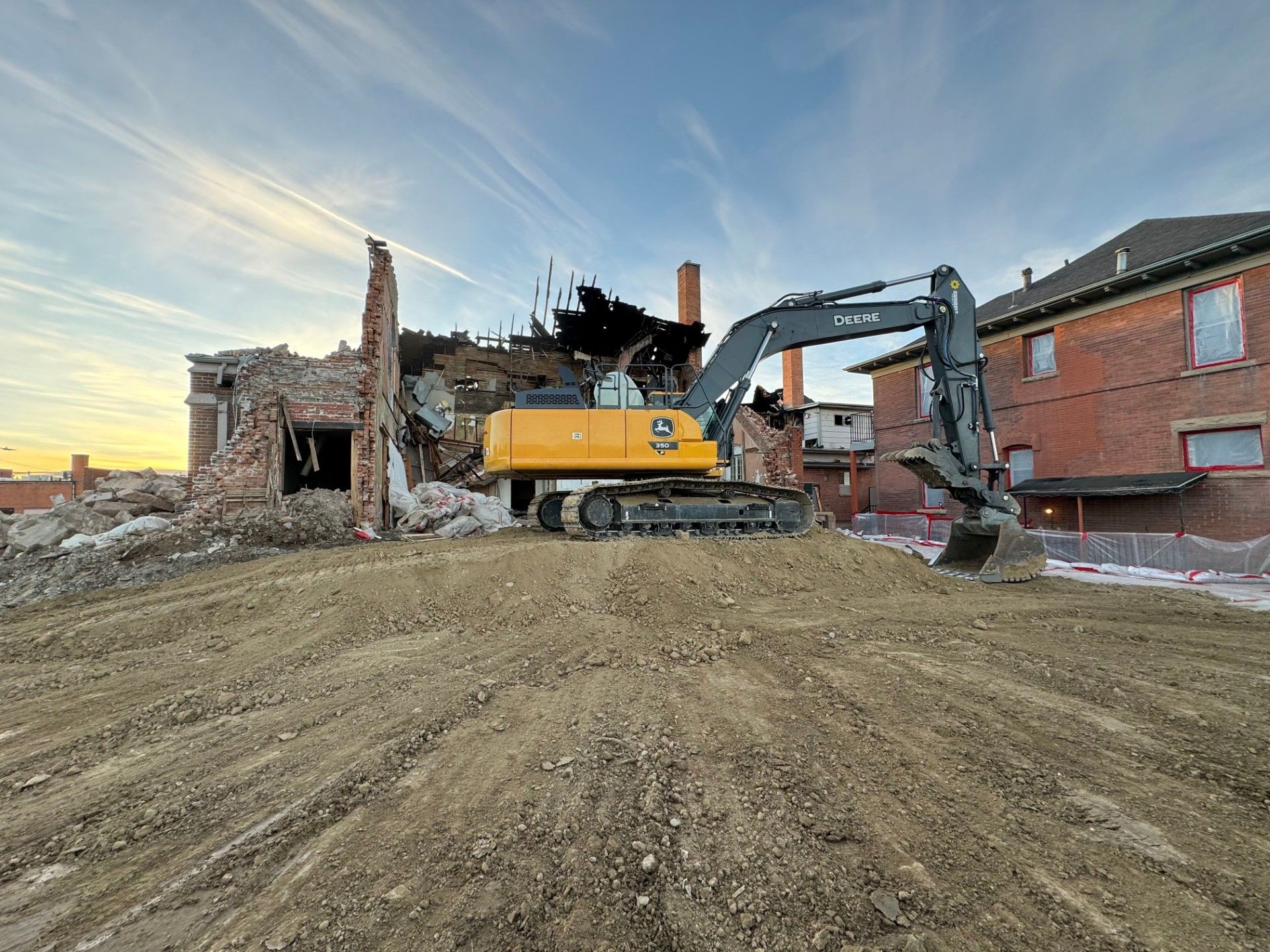 A large yellow excavator is demolishing a brick building