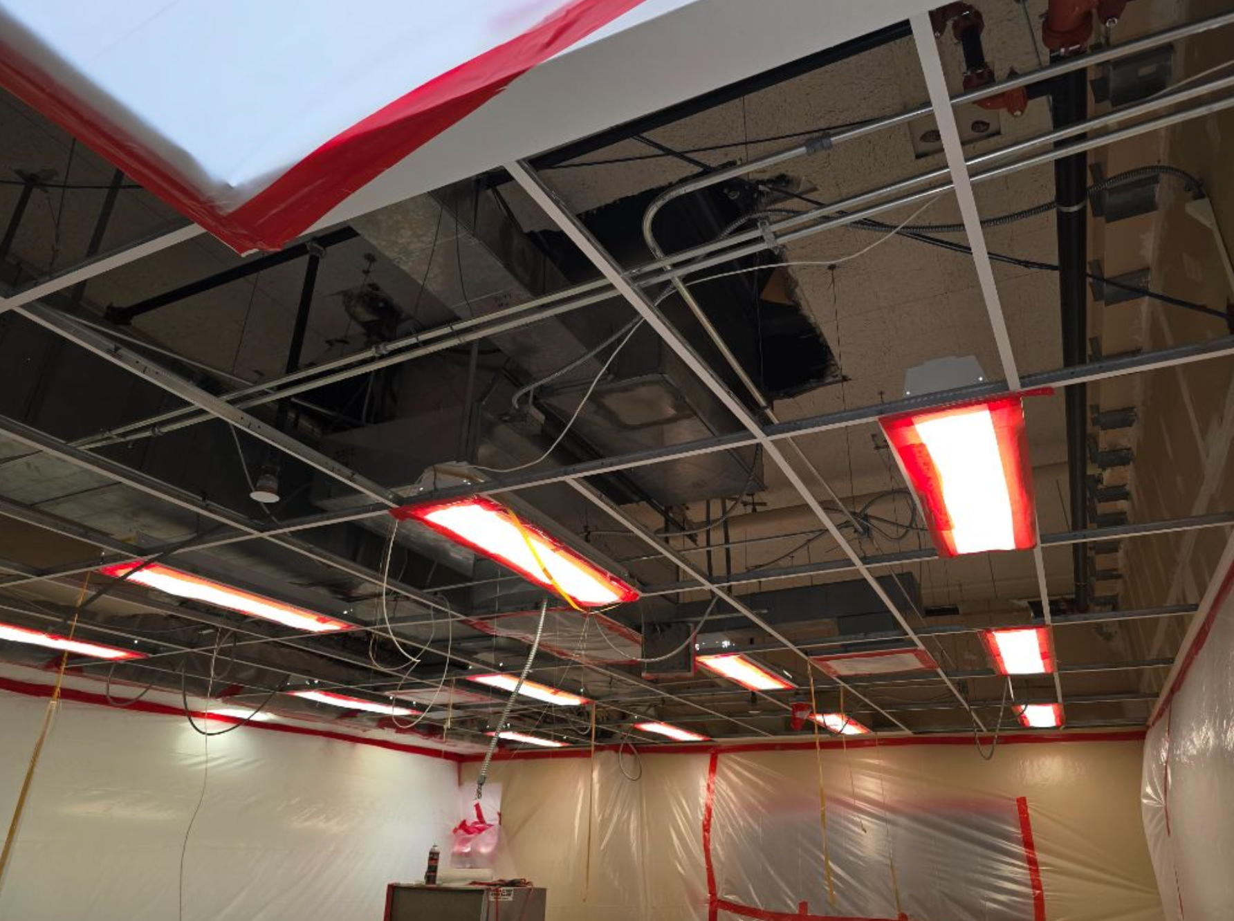 Construction site ceiling with red lights, ductwork, and plastic sheeting.