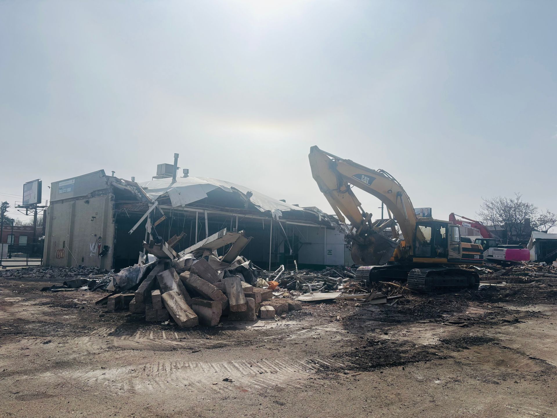 A large yellow excavator is demolishing a building in a field.