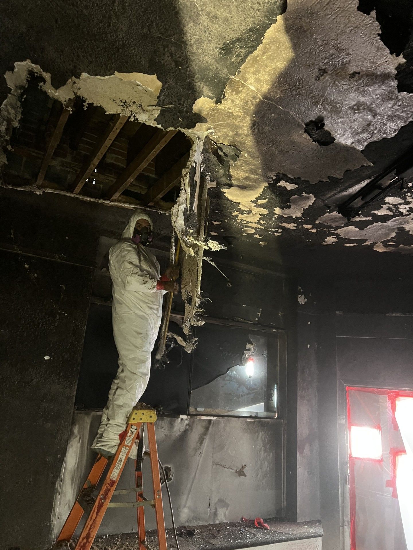 A man is standing on a ladder in a room with a hole in the ceiling.