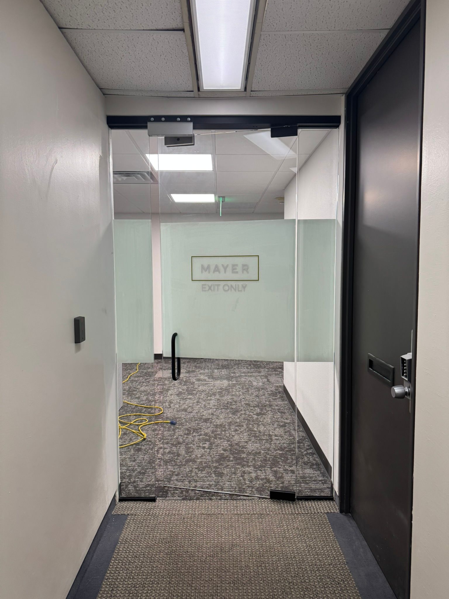 A hallway in an office building with a glass door leading to a room.