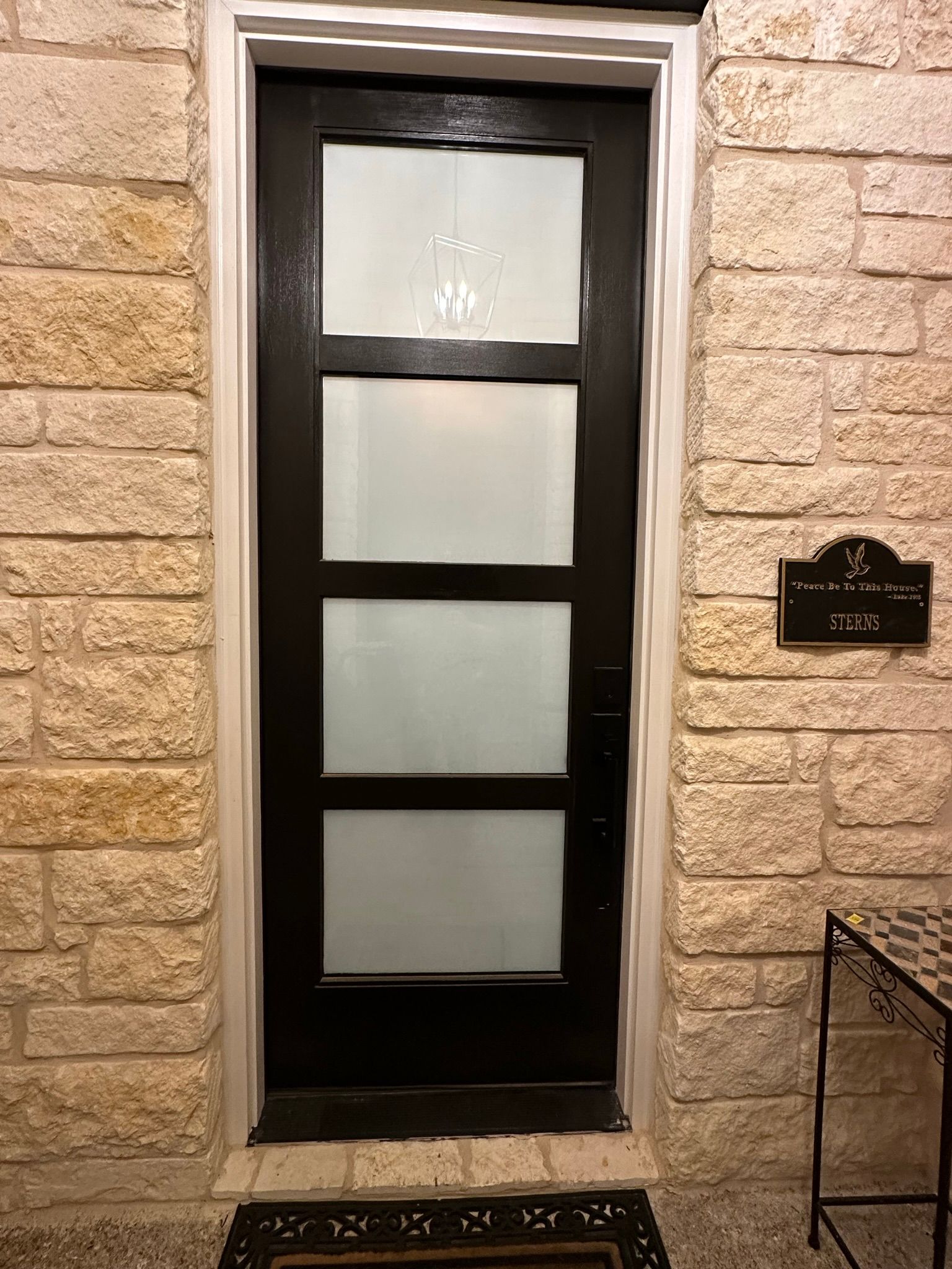 A black door with frosted glass is on a brick wall.