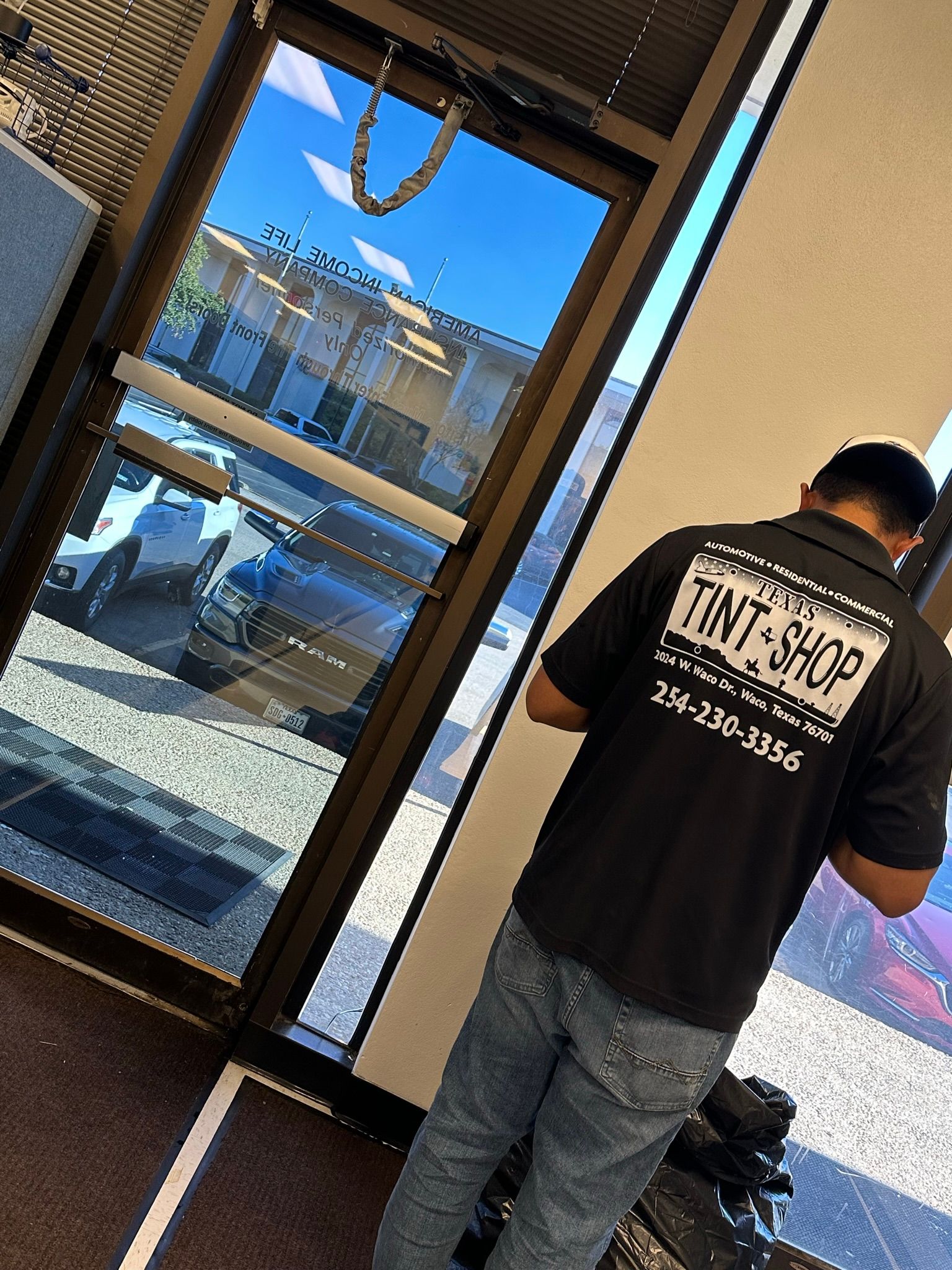 A man in a tint shop shirt is standing in front of a glass door.
