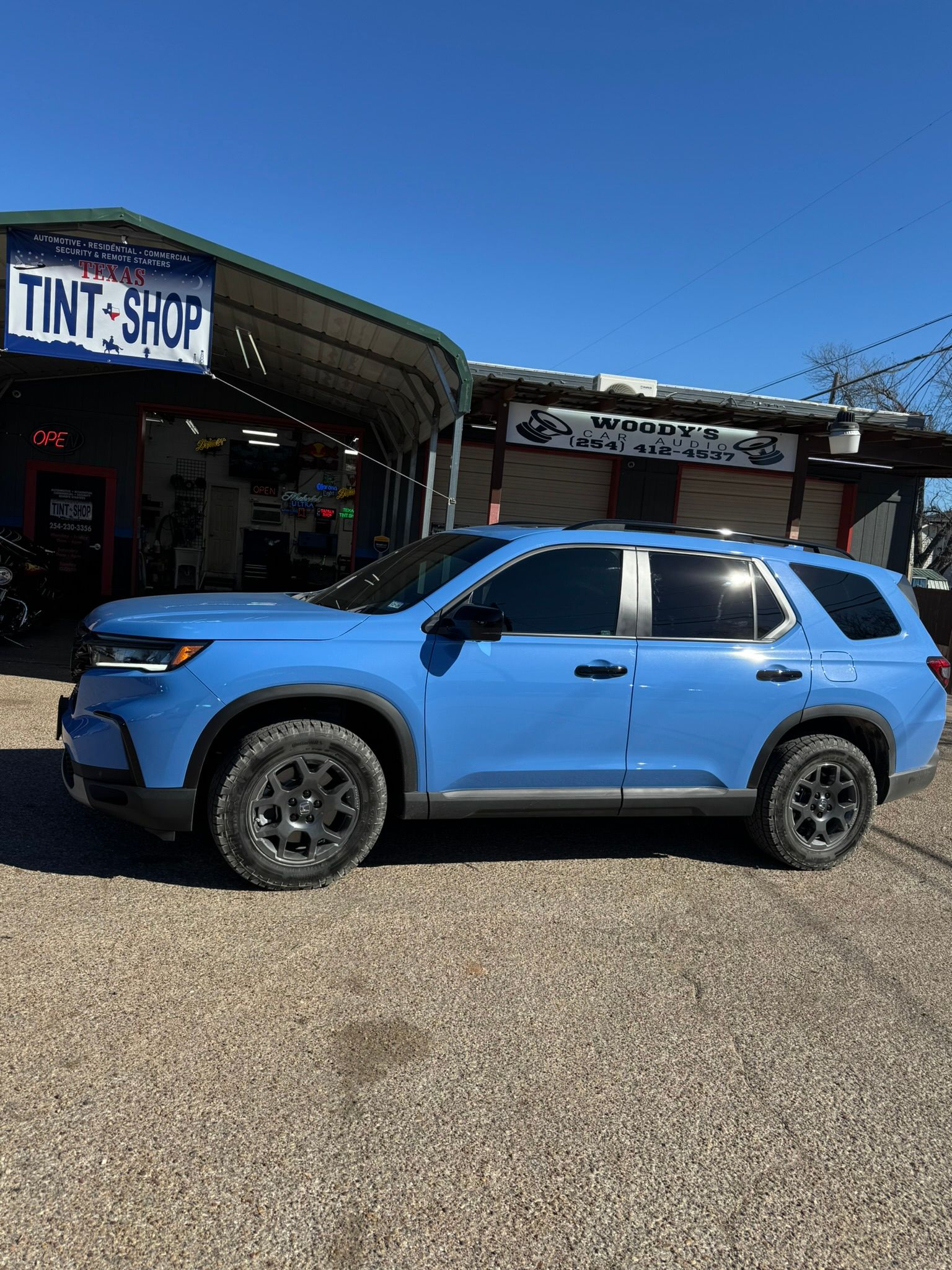 A blue suv is parked in front of a tint shop.