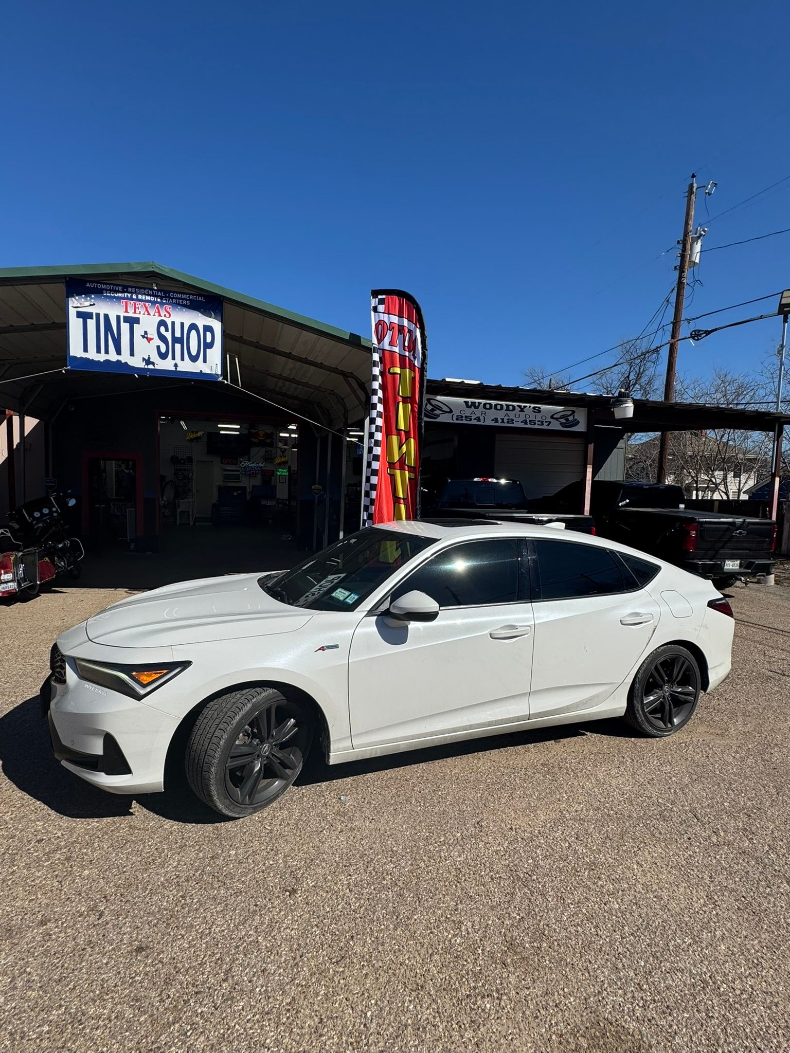 A white car is parked in front of a tint shop.