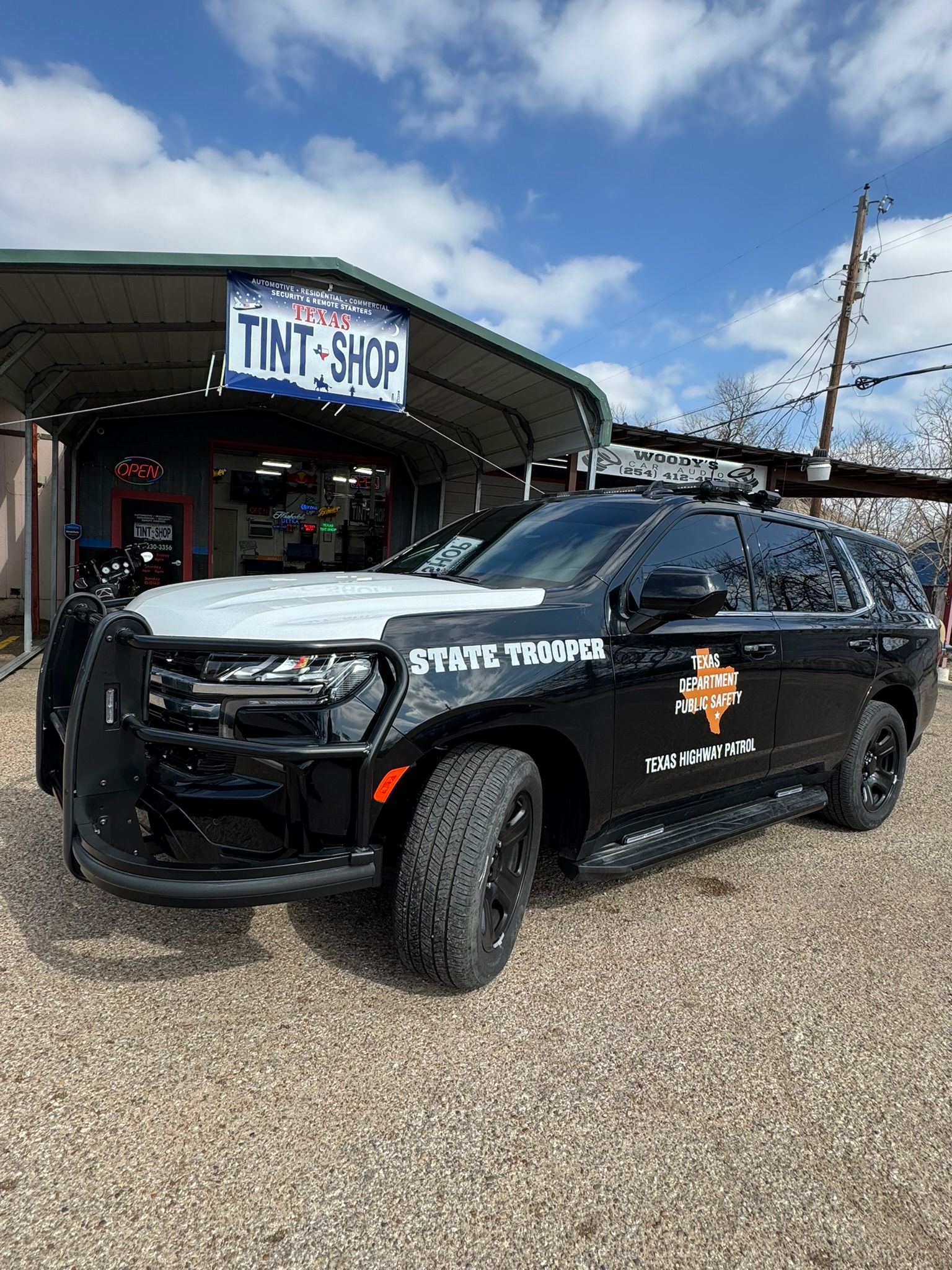 A black and white police car is parked in front of a tint shop.