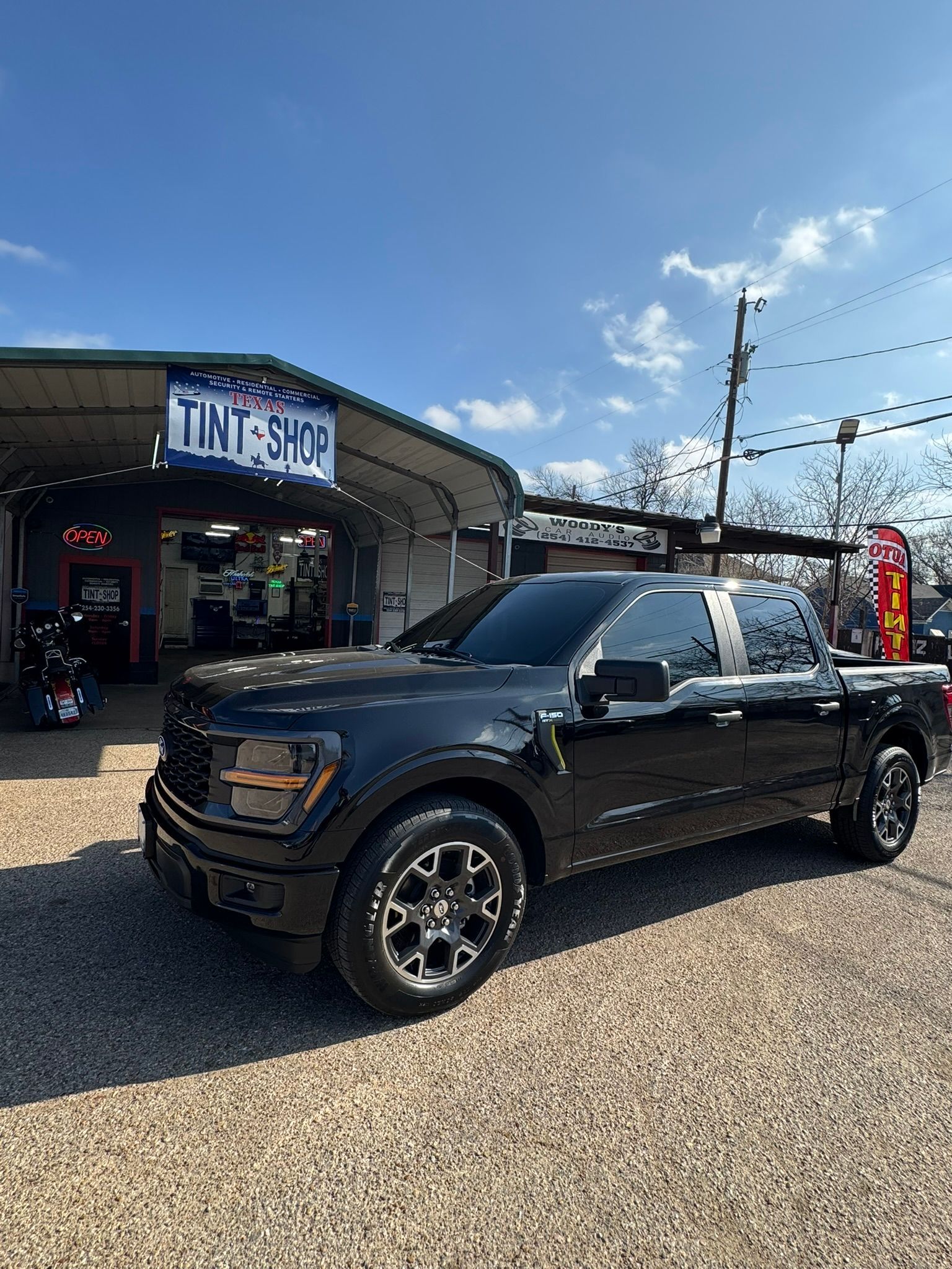 A black pickup truck is parked in front of a tint shop.