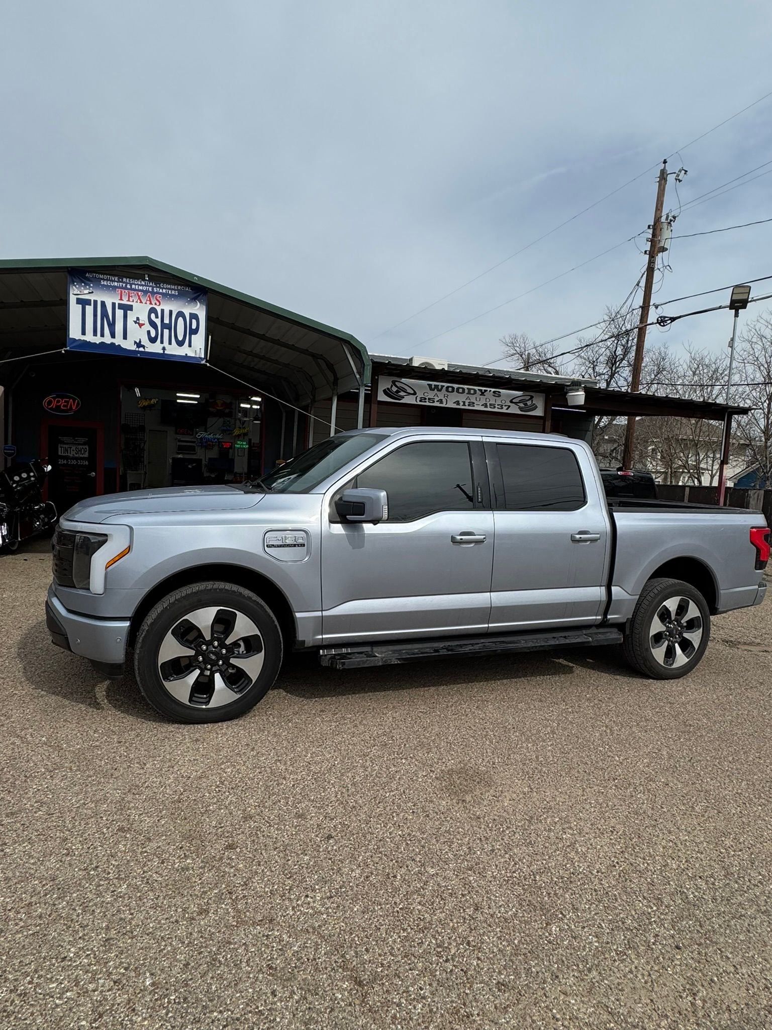 A silver pickup truck is parked in front of a tint shop.