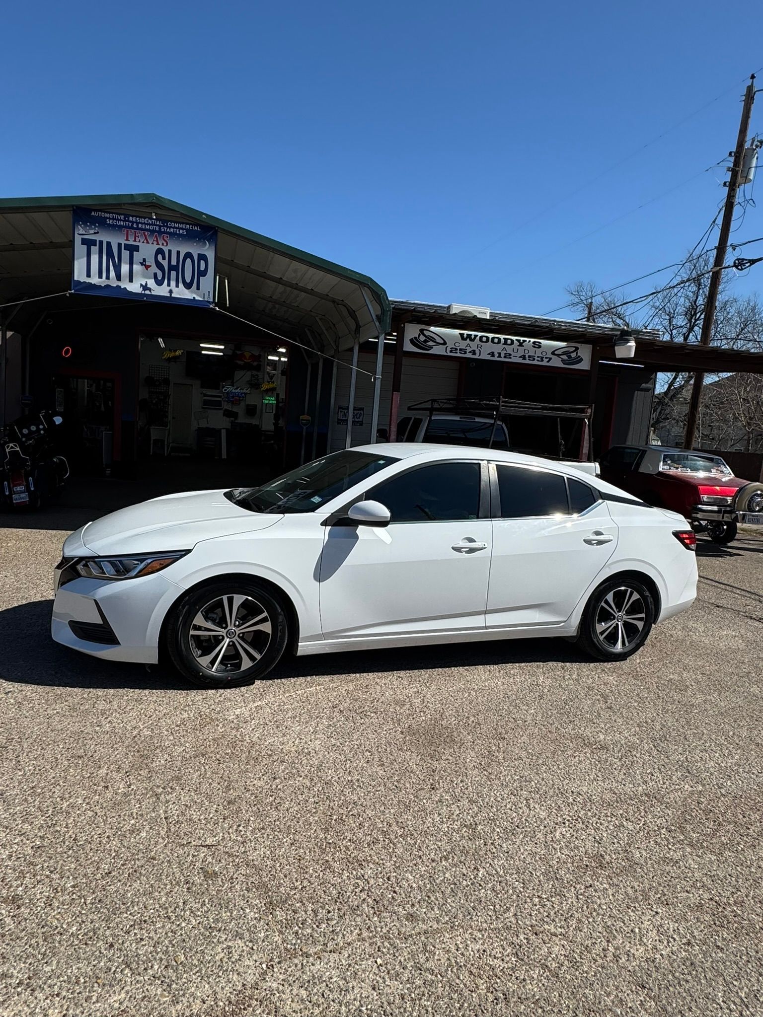 A white car is parked in front of a tint shop.