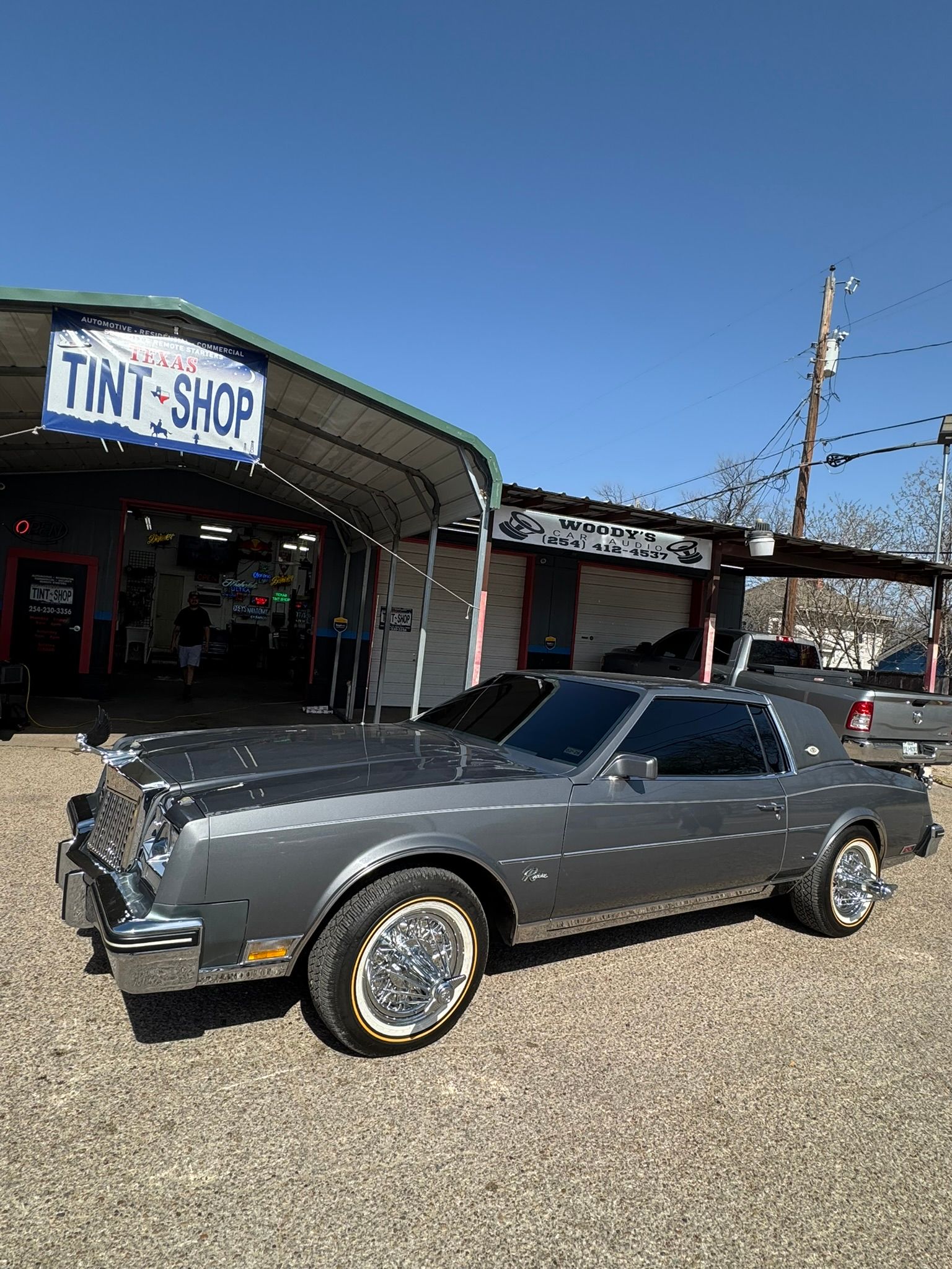 A gray car is parked in front of a tint shop.