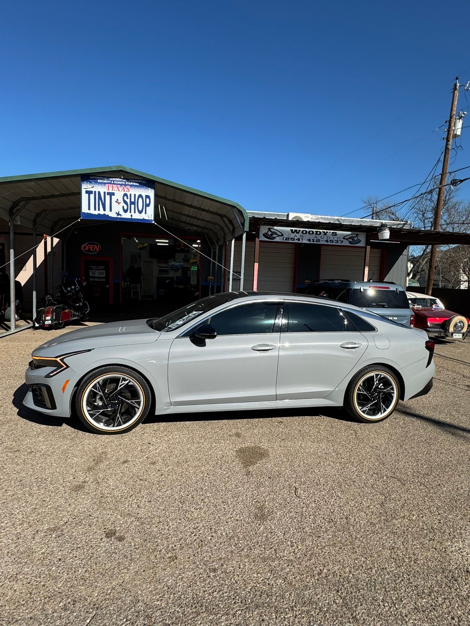 A silver car is parked in front of a tint shop.