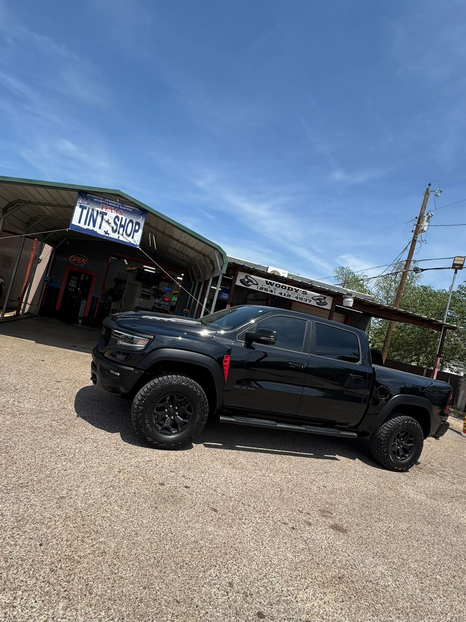 A black truck is parked in a gravel lot in front of a building.