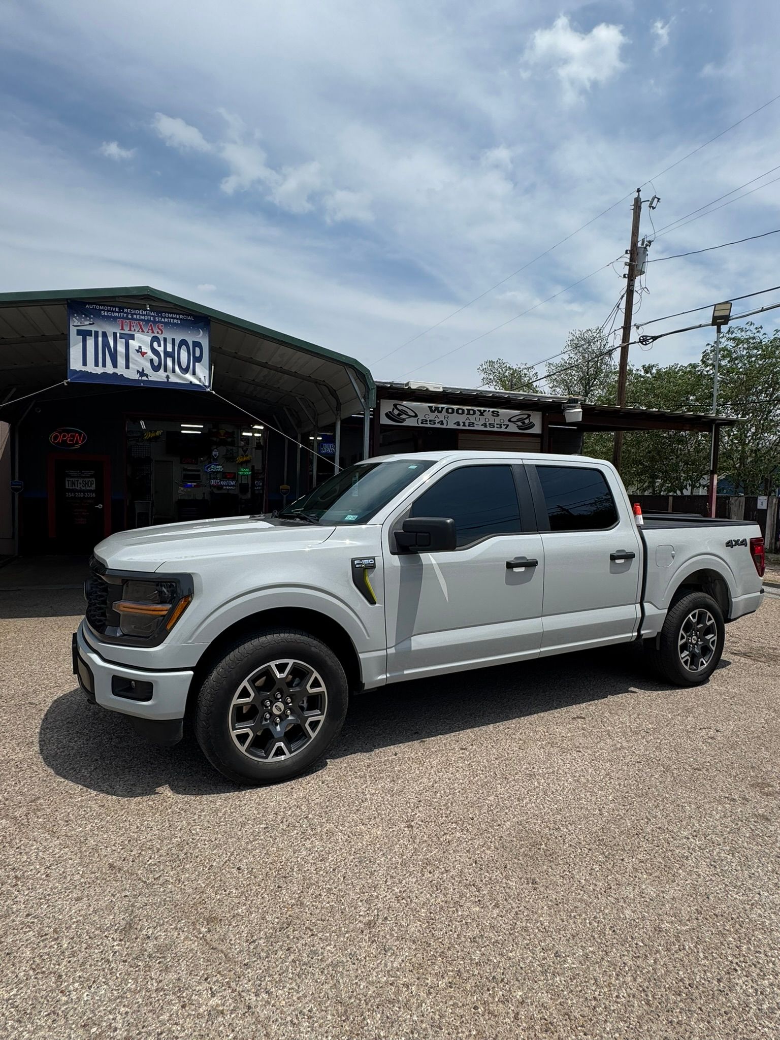 A white pickup truck is parked in front of a tint shop.