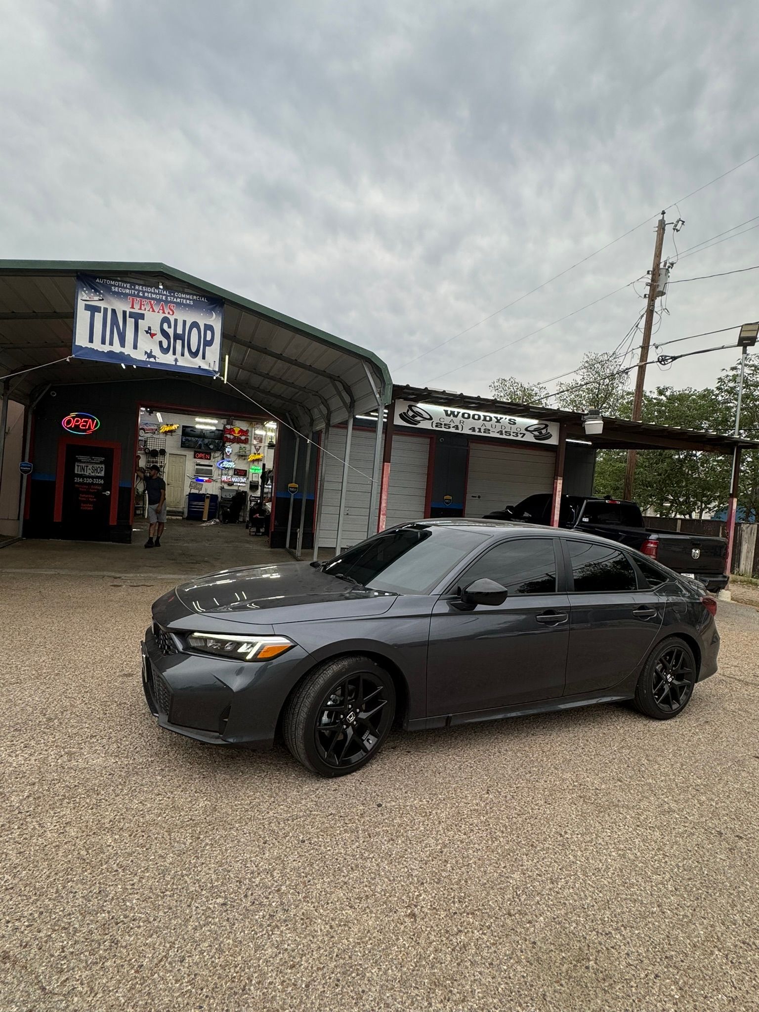 A gray car is parked in front of a tint shop.