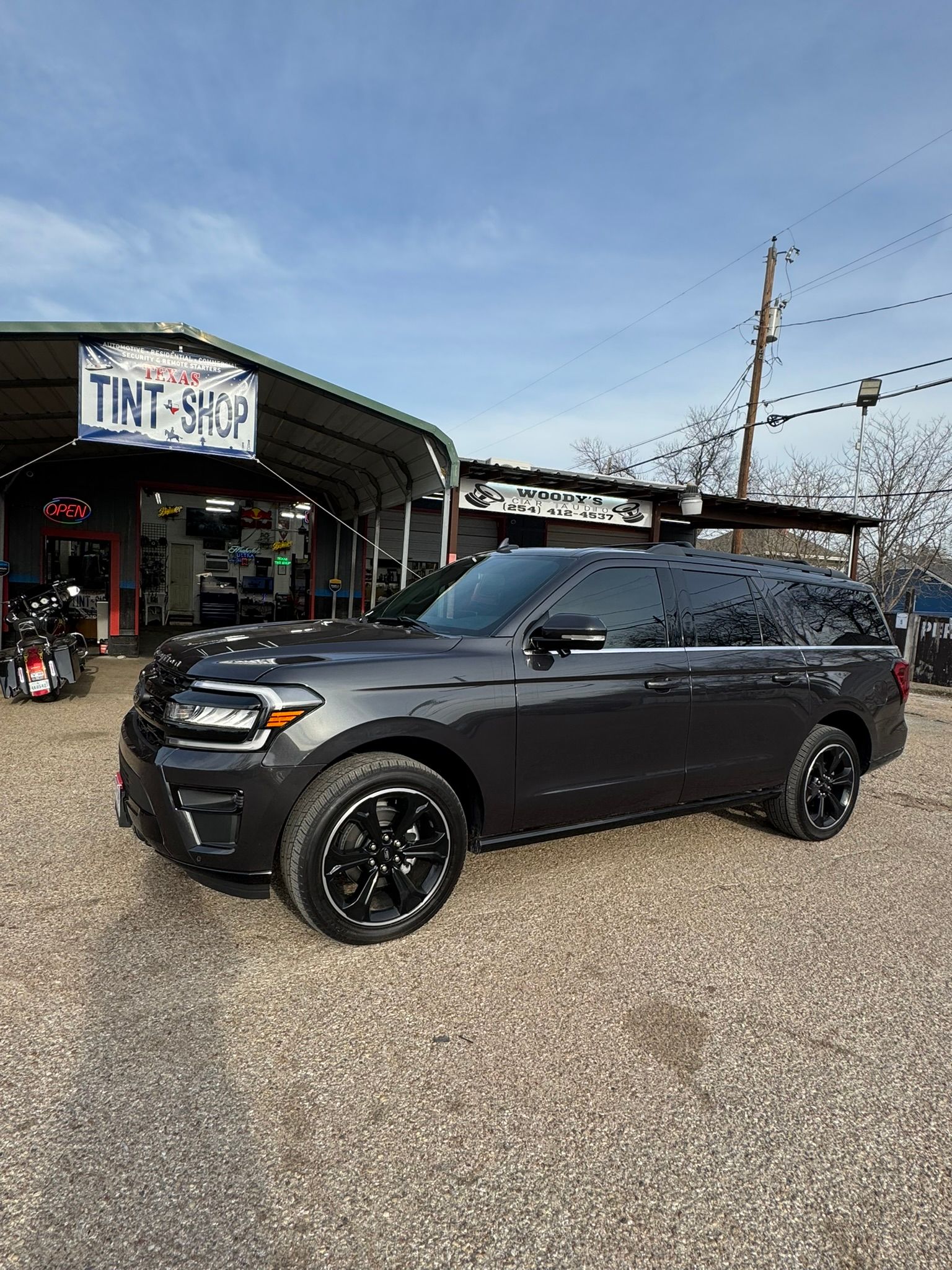 A black suv is parked in front of a building in a gravel lot.