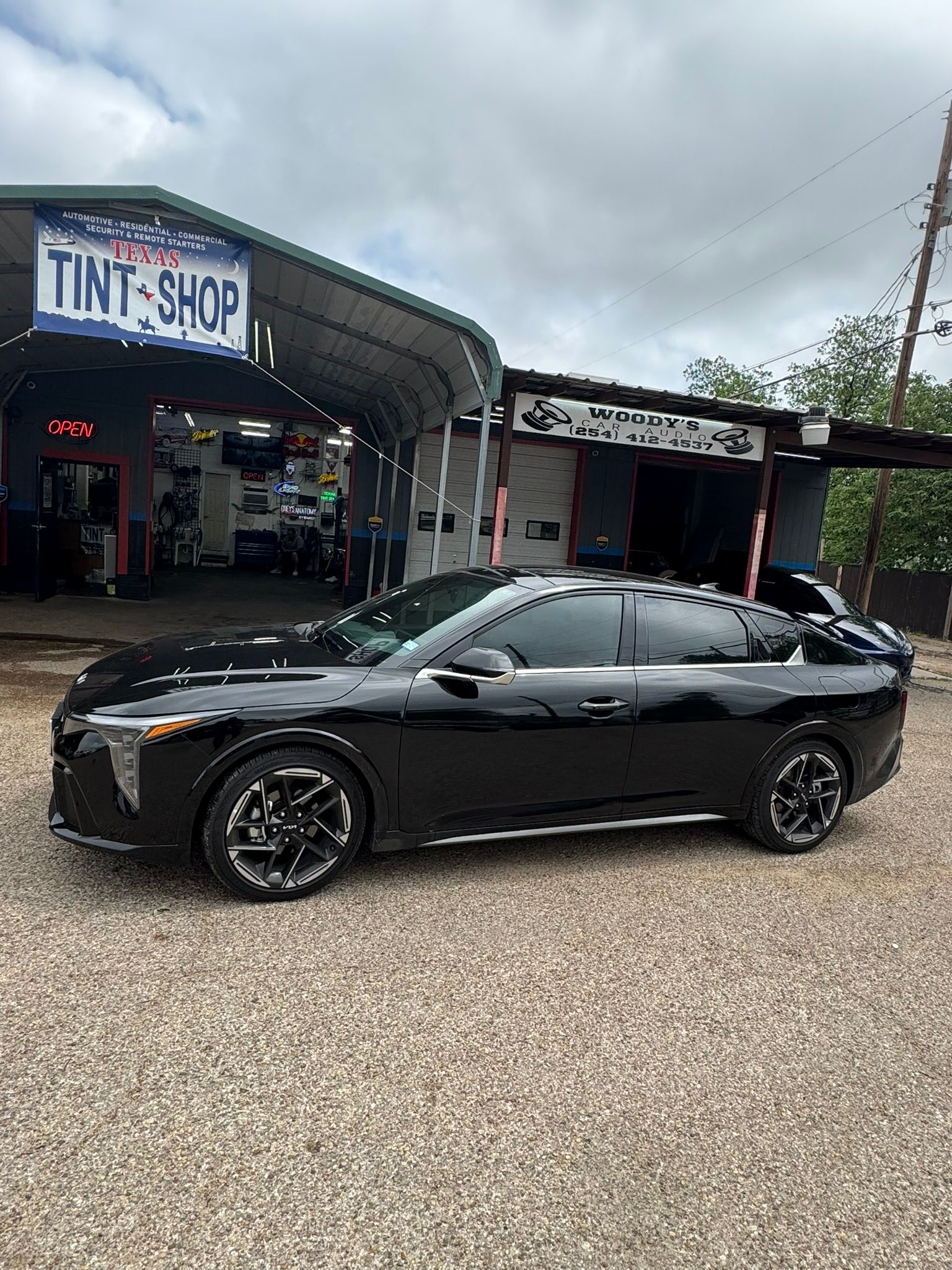 A black car is parked in front of a tint shop.